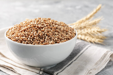 Wheat grains in bowl and spikes on grey table, closeup