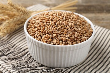 Wheat grains in bowl and spikes on table, closeup