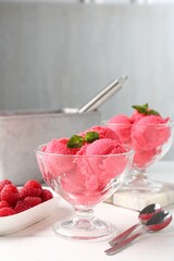Delicious raspberry sorbet with mint in dessert bowls, spoons and fresh berries on white wooden...