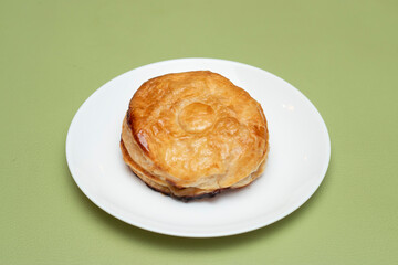 Baked chicken patty on a white plate with a flaky golden pastry crust side view of Bangladeshi food