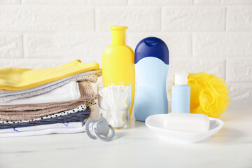 Different baby clothes and accessories on table near brick wall