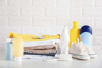 Different baby clothes and accessories on table near brick wall