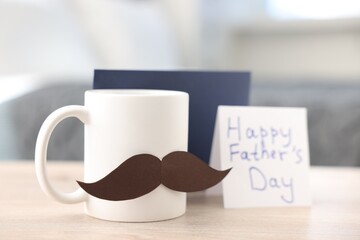 Happy Father's Day card, cup with mustache and envelope on wooden table at home, closeup