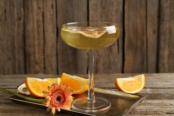 Martini cocktail in glass, orange slices and flower on wooden table, closeup