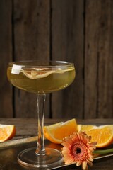 Martini cocktail in glass, orange slices and flower on wooden table, closeup