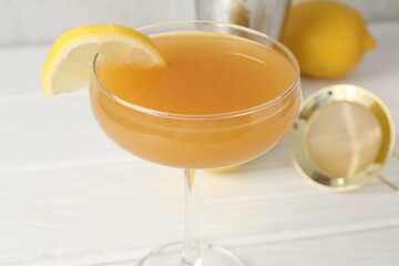 Martini cocktail with lemon slice in glass and fruit on white wooden table, closeup