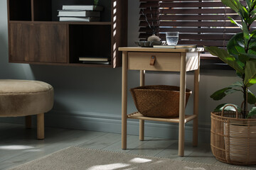 Wooden side table with glass of water, notebook, air reed diffuser and basket near window indoors