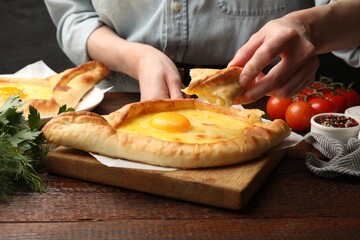 Woman eating delicious khachapuri at wooden table, closeup
