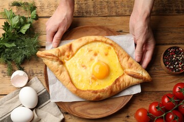 Woman with delicious khachapuri at wooden table, top view
