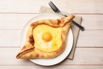 Tasty khachapuri with cheese, egg and fork on wooden table, top view