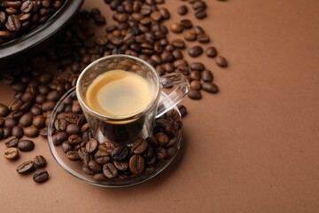 Cup of hot coffee and beans on brown background, closeup. Space for text