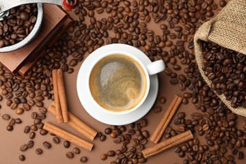 Cup of hot coffee, grinder, cinnamon and beans on brown background, flat lay