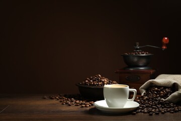 Aromatic coffee in cup, beans and grinder on wooden table against brown background, space for text