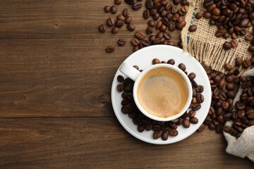 Aromatic coffee in cup and beans on wooden table, flat lay. Space for text