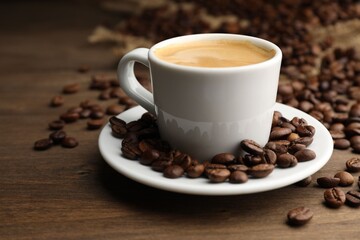 Aromatic coffee in cup and beans on wooden table, closeup