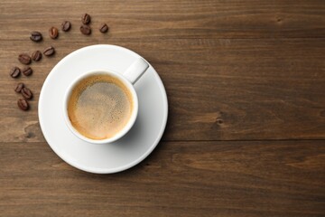 Aromatic coffee in cup and beans on wooden table, flat lay. Space for text