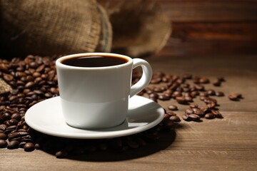 Aromatic coffee in cup and beans on wooden table, closeup. Space for text