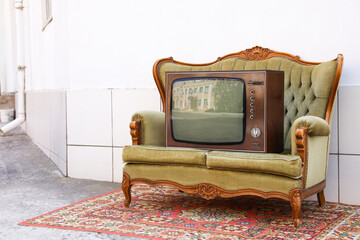 Retro TV on sofa and carpet near white wall outdoors. Used stuff