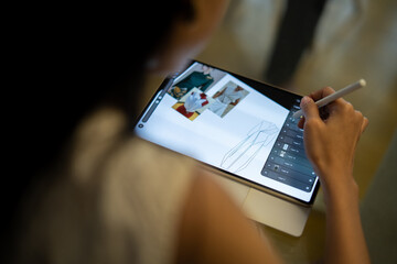 Close-up of a fashion designer sketching clothes on a digital tablet with stylus, creating modern dress design using digital drawing software.