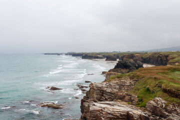 Turists visiting Cathedrals beach playa de las catedrales Spain Atlantic ocean. Natural rock arch on Cathedrals beach in low tide Cantabric coast, Lugo Galicia