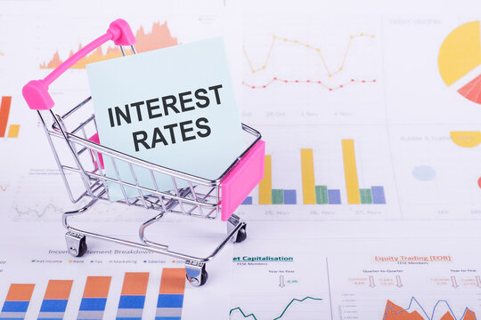 A pink shopping cart sits on a financial chart, carrying a blue note with the words INTEREST RATES written on it.