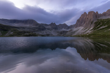 Fototapeta premium Reflective lake mirrors dramatic mountains under an overcast sky, a serene landscape