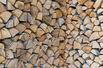 Stacked firewood logs forming an L-shaped pile, close-up view with selective focus, natural renewable energy and rustic background.