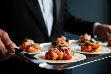 Waiter serving pasta dish from a silver tray
