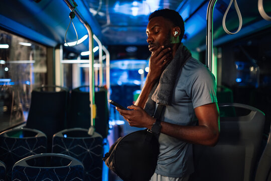 Tired black athlete using smartphone on bus after night training