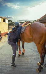 Young female rider gaining momentum to mount her horse outdoors before equestrian training at...