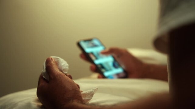 Man scroll porn sites and masturbate watching adult video on smart phone with only tissues around him. Loneliness man watching porn site video on bed.