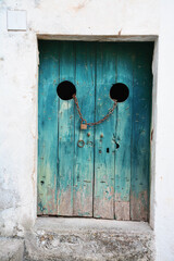 Vintage turquoise double doors with circular openings and padlock evoke mystery and intrigue