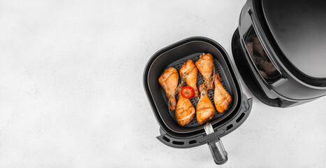 Cooked chicken drumsticks in air fryer basket with tomato and herbs. top view. copy space