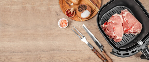 Raw pork chops with spices and utensils near air fryer on wooden table. top view. copy space