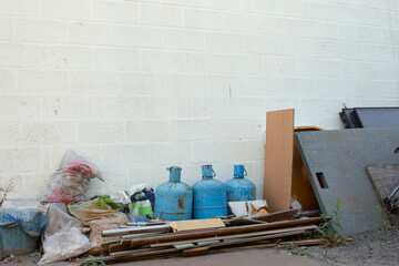 Old blue gas cylinders and mixed construction waste stacked near a white brick wall. The image...