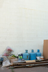 Piles of construction debris, plastic bags, and three old rusty gas cylinders leaning against a...