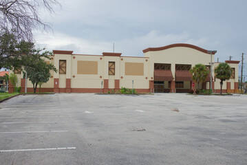 Vacant Commercial Grocery Building Exterior in Sunny Weather With Parking Lot. Closed property features an empty parking lot and tropical landscaping under a blue sky. The image communicates concepts 