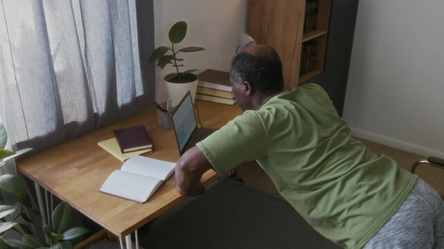 Medium rear shot of fit mature African American man oing press-ups against des, while taking break from orking on presentation or usiness report on laptop cmputer at home