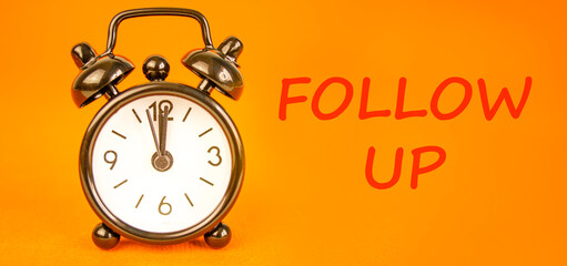 Follow up symbol. Concept word Follow up on beautiful orange paper. Beautiful black alarm clock....