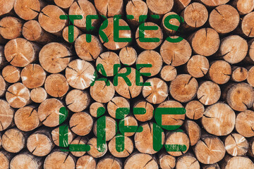 Environmental concept with stacked cut logs and bold green text saying "Trees Are Life", highlighting deforestation issues, nature conservation, and the importance of forests for human survival.