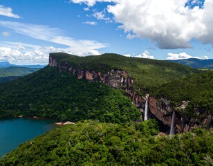 Lush green mountains and a waterfall cascading down a rocky cliff face overlooking a lake, a clear blue sky above
