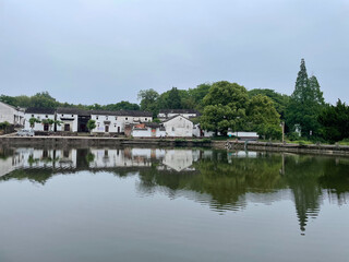 Fototapeta premium Traditional Chinese village with serene lake reflection under a cloudy sky.