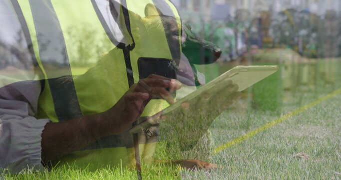 Kneeling handler and German Shepherd wearing reflective vests using tablet on field, painted line - Powered by Adobe