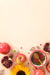 Flat lay of apples, honey, pomegranates, sunflower, and autumn flowers on beige background. Rosh Hashanah Jewish holiday concept.