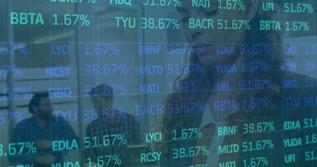 Woman wearing suit and eyeglasses viewing stock tickers on transparent screen in office, copy space
