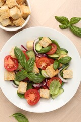 Delicious salad with croutons, vegetables and basil on wooden table, flat lay