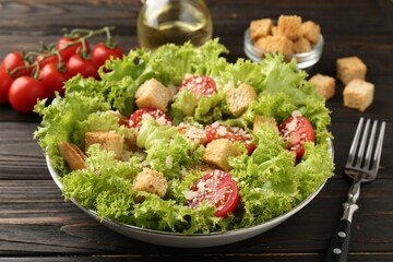 Tasty salad with croutons, tomatoes, cheese and chicken on black wooden table, closeup
