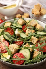 Tasty salad with croutons, cucumbers, tomatoes and arugula on wooden table, closeup