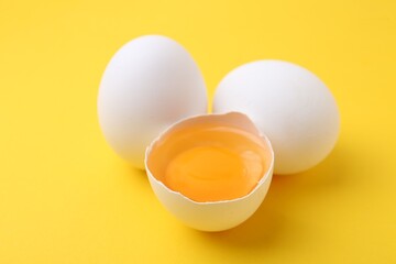 Whole and broken chicken eggs on yellow background, closeup