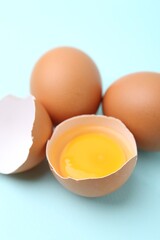 Whole and broken chicken eggs on light blue background, closeup